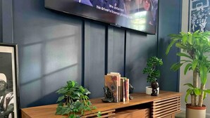 Un salon moderne avec un meuble de rangement en bois pour l’équipement audiovisuel, un téléviseur fixé au mur et divers objets décoratifs, notamment des livres et des plantes.