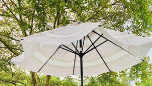 Une table ronde en verre, six chaises, un parasol et un tapis à motifs sur une terrasse en bois.