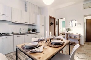 A modern kitchen with white cabinets, a dining table set with plates, glasses, and a candle. - Il Lauro - My Home in Como (Como)