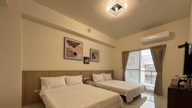 Habitación de hotel con dos camas, una ventana con cortinas, una lámpara de techo y obras de arte colgadas en la pared.