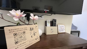 Un mostrador de recepción de madera con un código QR, un control remoto y un cartel de bienvenida.
