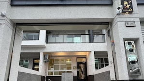 Un edificio moderno con un acceso de dos pisos, una alarma de incendios visible y un cartel con caracteres chinos.