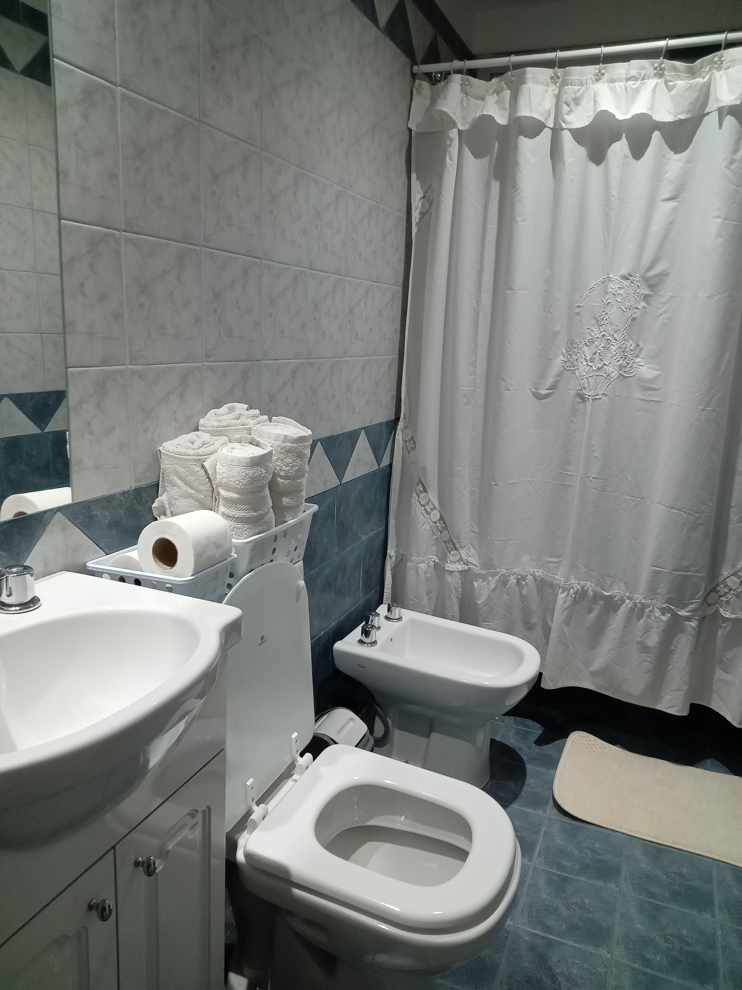 A bathroom with a sink, toilet, bidet, and a shower curtain.