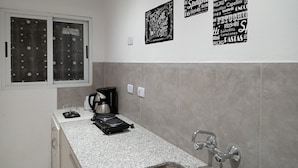 A kitchen with a granite countertop, a coffee maker, and a sink. There are three black signs on the wall with Italian words. - Consorcio General Acha ,apartamentos (San Juan)