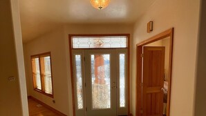 Un corridoio con pavimento in legno, una porta in vetro con motivo decorativo e un lampadario al soffitto.