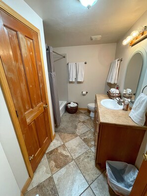 A bathroom with a wooden door, a white bathtub, a toilet, a sink, and a mirror. - Family Lodge in Beautiful Star Valley (Star Valley Ranch)