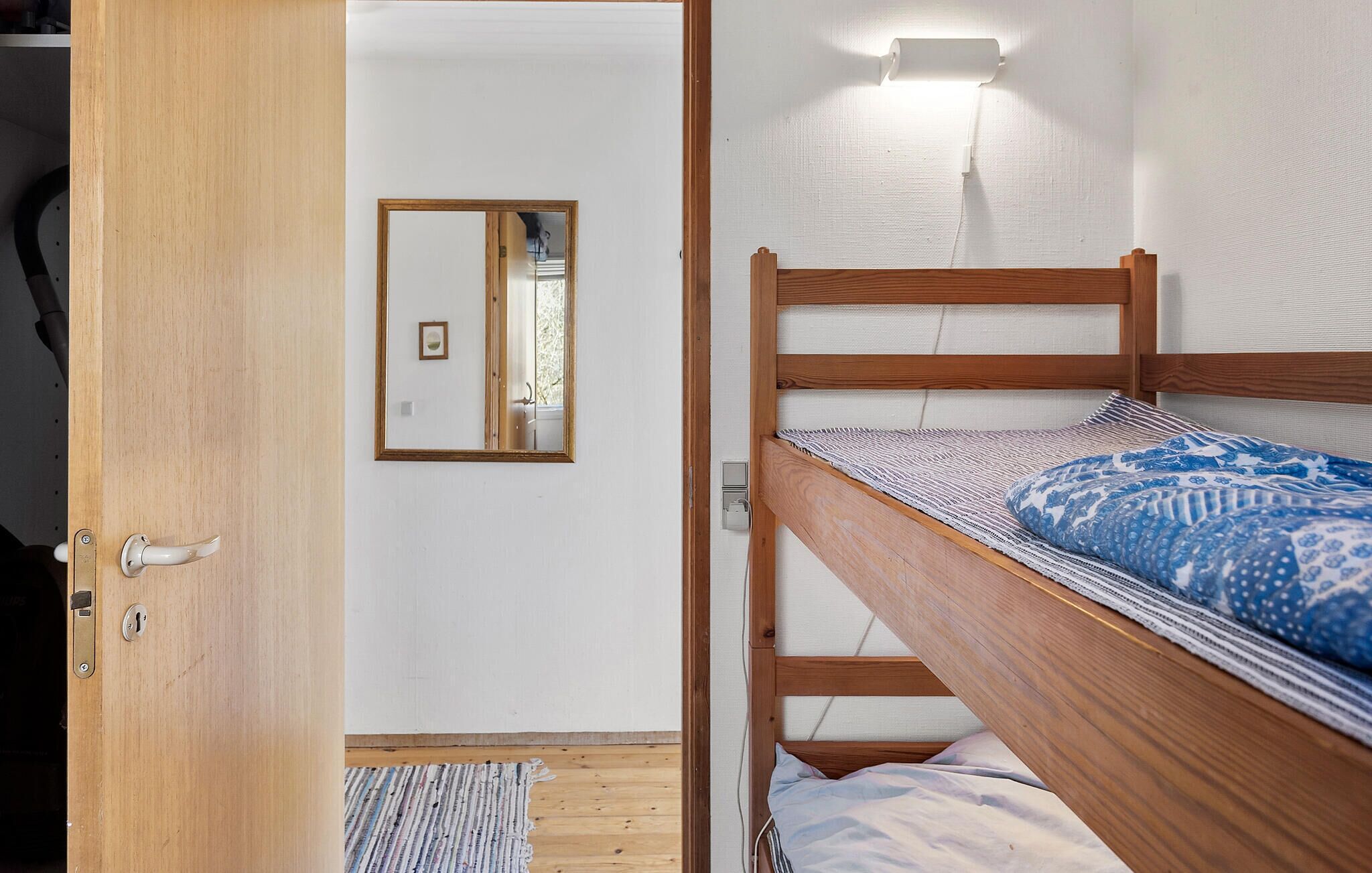 Ein Zimmer mit einem Etagenbett, einer Holztür, einem Spiegel und einer Wandleuchte.