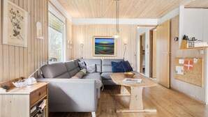 Un salon chaleureux avec un canapé gris, un parquet en bois et un tableau représentant un paysage.