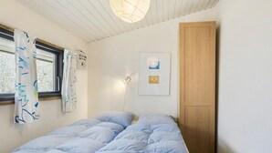 Une chambre avec un lit simple, une armoire en bois, une fenêtre avec des rideaux et un luminaire fixé au mur.