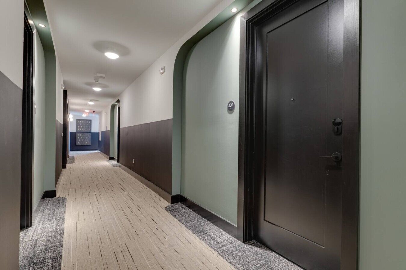 A hallway with a carpeted floor, doors on both sides, and a light fixture on the ceiling.