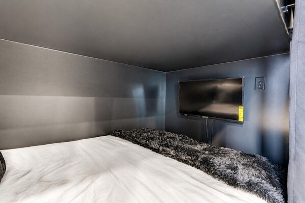 A room with a bed, a flat-screen TV mounted on the wall, and a control panel.