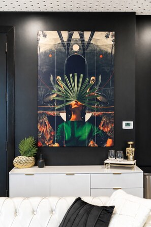 Una habitación con un cuadro abstracto grande en la pared, una consola blanca decorativa y un sofá blanco capitonado.
