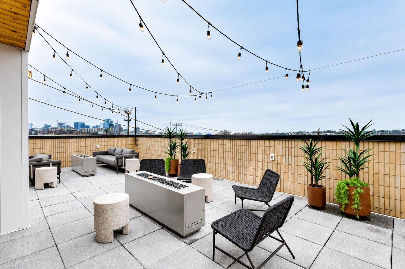 A rooftop patio with outdoor furniture, a fire pit, string lights, and potted plants.