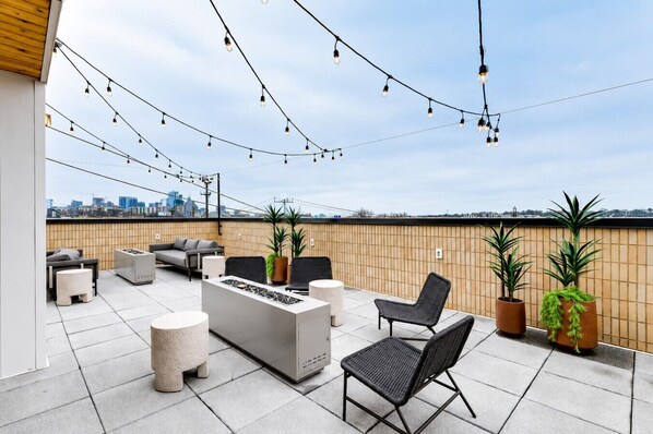 Terraza en la azotea con mobiliario exterior, una chimenea, luces colgantes y plantas en macetas.