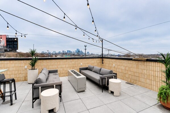 Terraza en la azotea con mesas al aire libre, luces colgantes y vista al horizonte urbano.