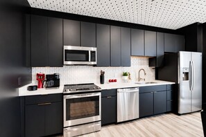 A modern kitchen with dark cabinetry, stainless steel appliances, and a white tiled backsplash.