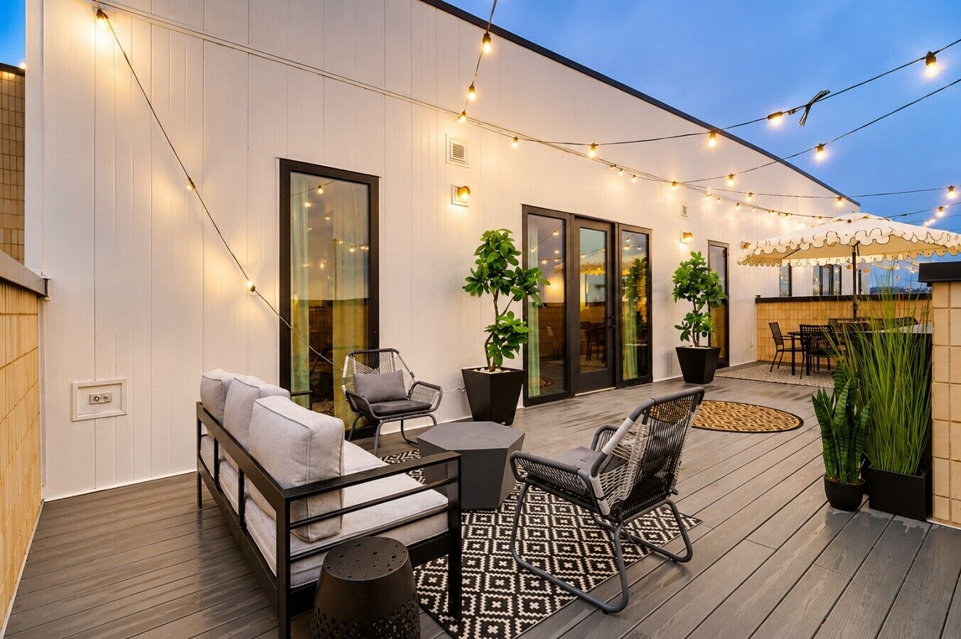 An outdoor patio with a sofa, chairs, a table, string lights, and potted plants.