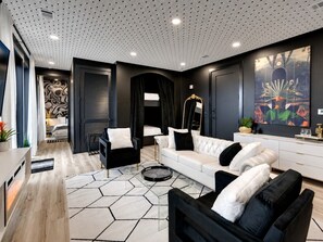 Una sala de estar moderna con un sofá blanco, sillones negros, una mesa de centro de vidrio y un tapete con motivos hexagonales.