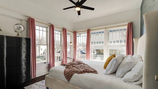 A bedroom with a bed, a dresser, a ceiling fan, and large windows. - Sleeps 8 Historic loft near 12 South with easy access to local attractions (Nashville)