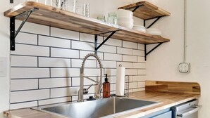 A kitchen with a wooden countertop, a stainless steel sink, and a black faucet. There are shelves above the sink holding glassware and jars. - Sleeps 8 Historic loft near 12 South with easy access to local attractions (Nashville)