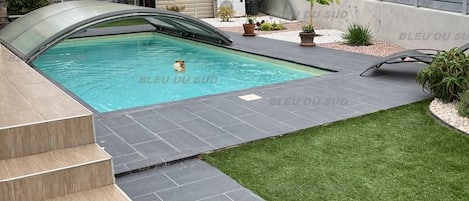 A swimming pool with a curved edge, surrounded by a well-maintained lawn and a stone deck.