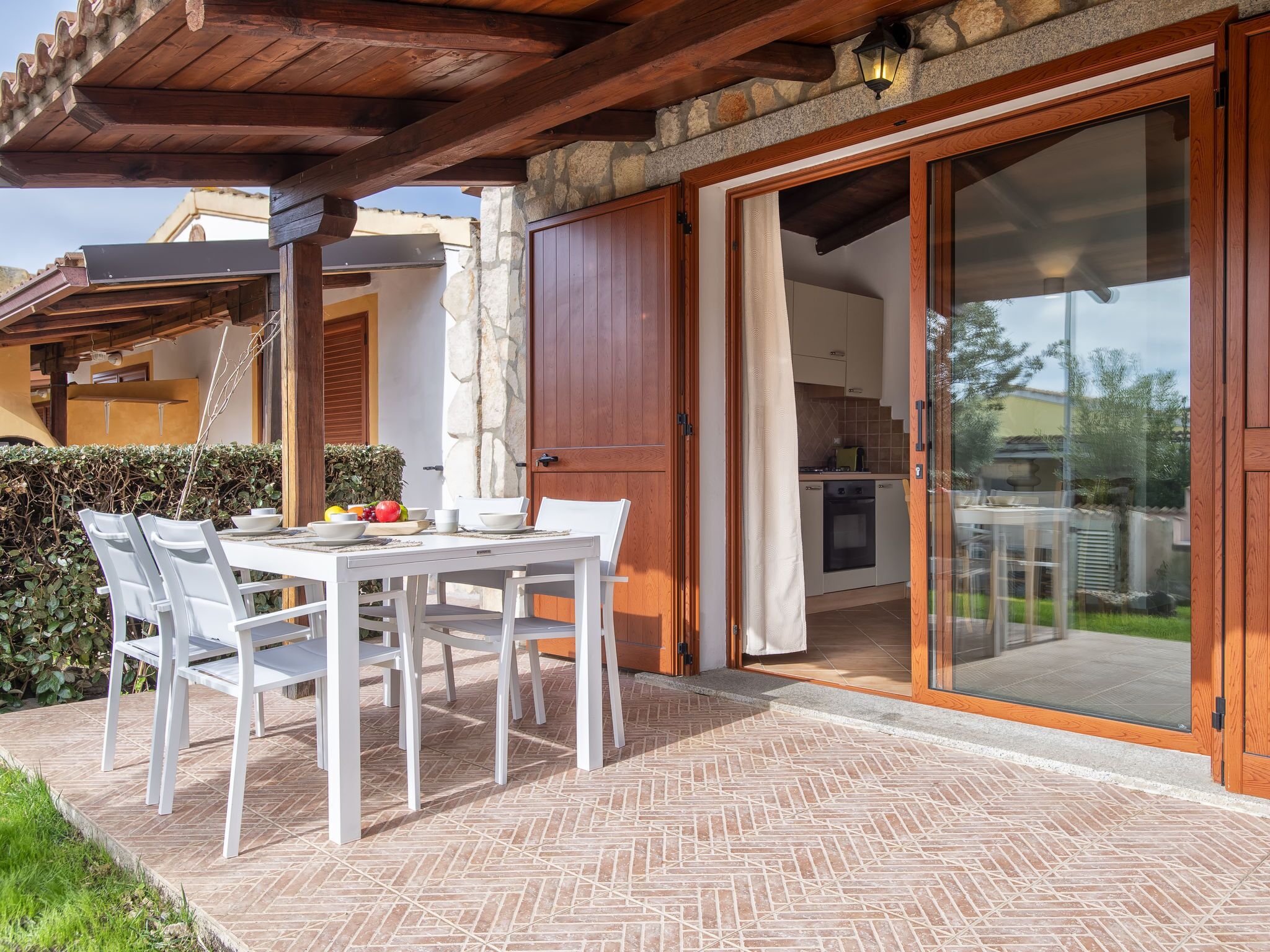 A patio with a table and chairs, a stone wall, and a sliding glass door leading to a kitchen.
