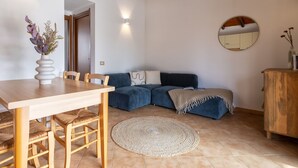 A dining area with a wooden table and chairs, a blue sofa, a round woven rug, and a wooden cabinet. - Vacation home Momo by Interhome (Valledoria)