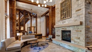 A spacious lobby with a stone fireplace, wooden beams, a staircase, and a seating area with sofas and a coffee table. - Luxury Amenities in Canyons!  Ski-in/Ski-out, Amenities, In-room dining (Park City)