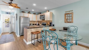 A kitchen with a central island, bar stools, and a glass dining table. - Perdido Dunes 30 2/2 sleeps 6 (Orange Beach)