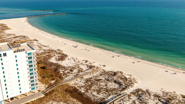 A beach with a white building, clear blue water, and a sandy shore. - Perdido Dunes 30 2/2 sleeps 6 (Orange Beach)