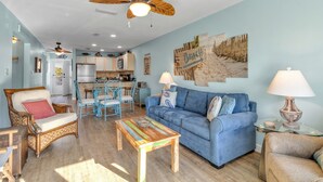 A living room with a blue sofa, a wooden coffee table, wicker chairs, and a ceiling fan. - Perdido Dunes 30 2/2 sleeps 6 (Orange Beach)