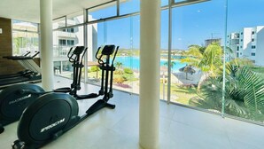 Un gimnasio con equipo de cardio y vistas a una piscina y palmeras.