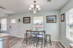 Un coin repas comprenant une table et quatre tabourets, un lustre et deux tableaux encadrés accrochés au mur.