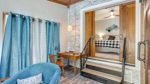 Una habitación acogedora con un sillón azul, un escritorio de madera y una escalera que conduce a un dormitorio con edredón de cuadros.