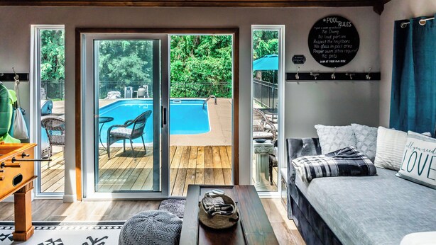 Un dormitorio con una cama grande, una mesa de madera y vistas a una piscina exterior a través de puertas de cristal.