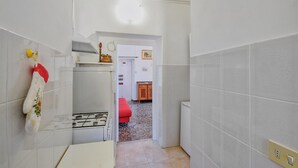 Un couloir étroit aux murs recouverts de carreaux blancs, avec un poêle blanc et, au fond, une chaise rouge.