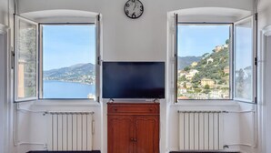 Une pièce avec une grande fenêtre, une horloge et un téléviseur posé sur un meuble en bois.