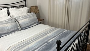 A neatly made bed with striped bedding, a metal headboard, and a wooden nightstand with a lamp.