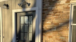 A house with a dark front door, a small porch with a potted plant, and a stone wall adjacent to the door.