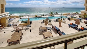Un espace aménagé au bord de la piscine, avec des chaises longues et des parasols, une piscine et une vue sur l’océan.