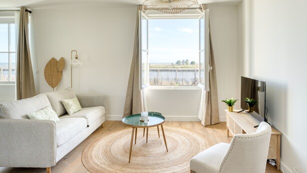Ein modernes Wohnzimmer mit einer Couch, einem Couchtisch, einem Fernseher und Blick auf das Meer durch ein großes Fenster.