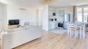 Ein modernes Wohnzimmer mit Sofa, Fernseher und Essbereich mit Stühlen und Tisch.