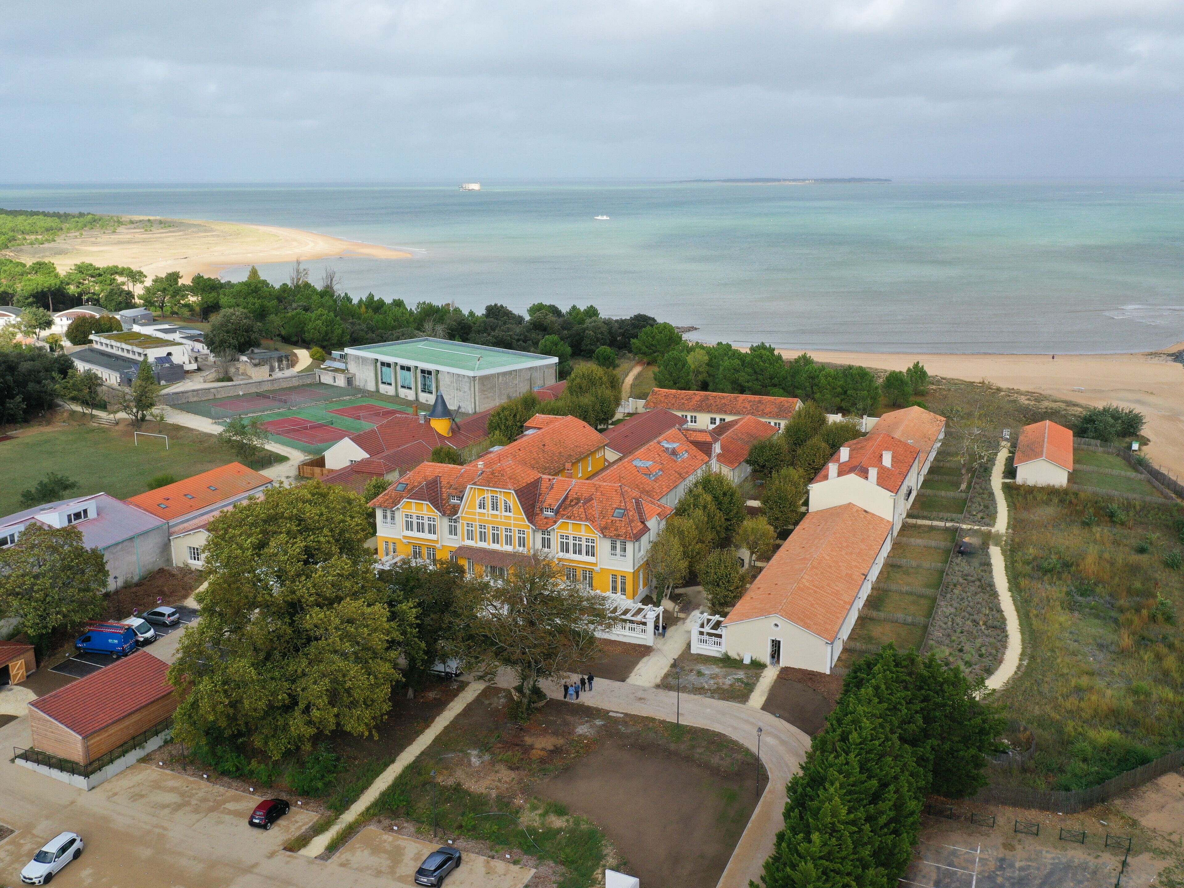An aerial view of a coastal residential area with houses, a beach, and a clear view of the sea.