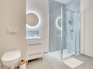 Enjoy a refreshing shower in the sleek shower with handheld showerhead and faucet, accompanied by a convenient vanity with round mirror and soap dispensers.