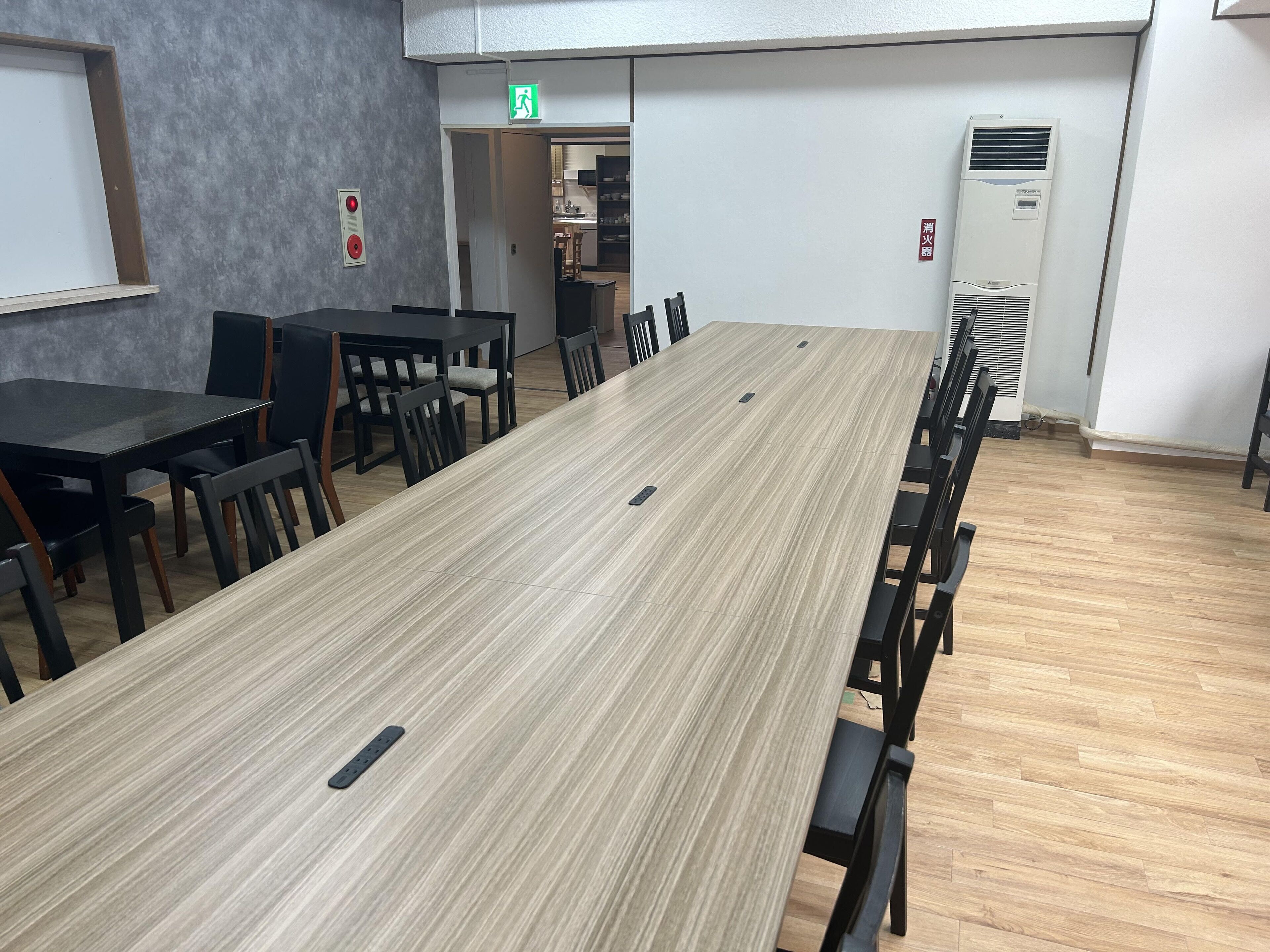 A conference room with a long table and chairs, a fire alarm, and an exit sign.