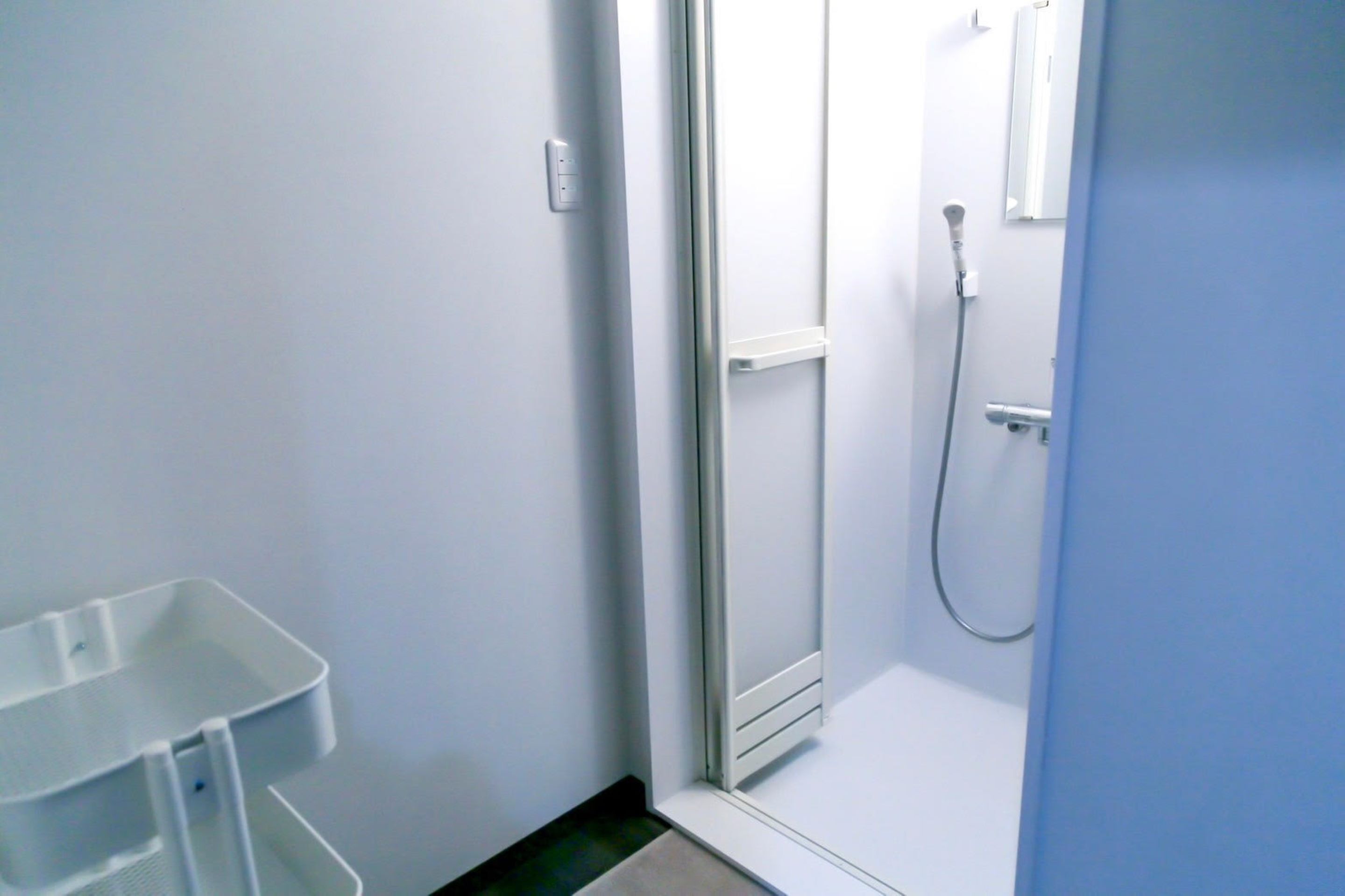 A bathroom with a shower, a white sink, and a white trash bin.
