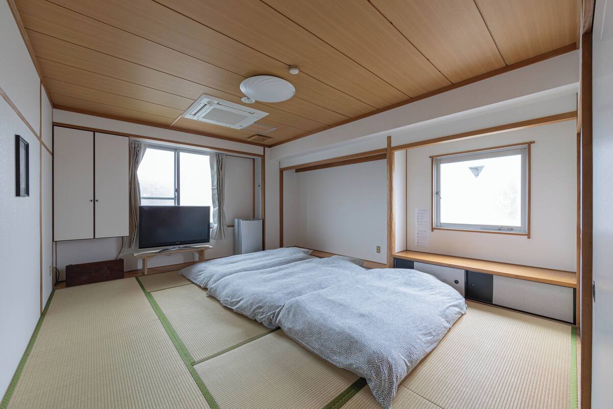 Een kamer met tatami matten, een bed, een televisie en een raam.