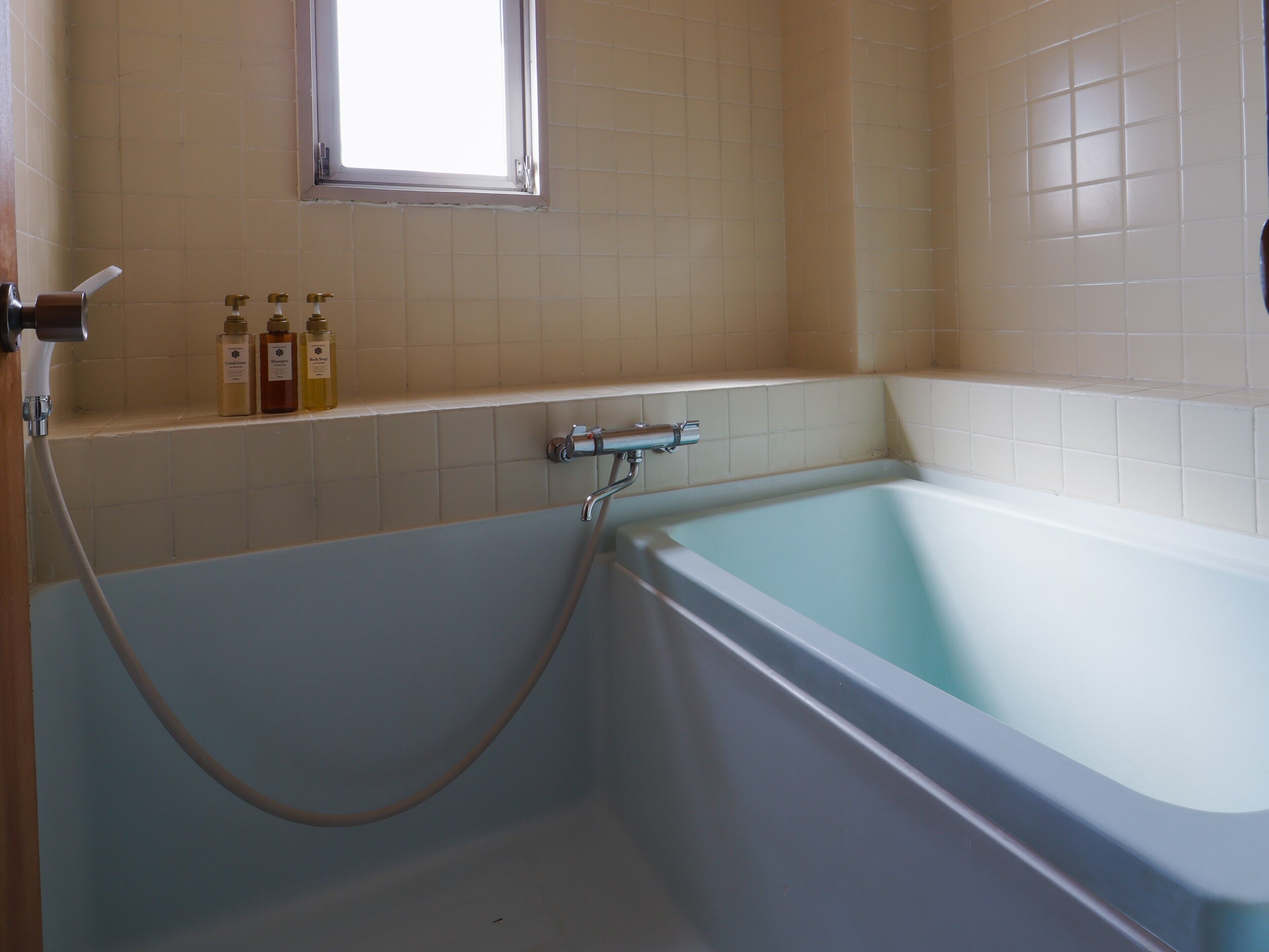 A bathroom with a bathtub, a window, and a shelf with toiletries.