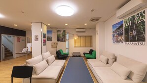A hotel lobby with a reception desk, two sofas, a small table, and a blue carpet. - Hostel JAQ takamatsu (Takamatsu)