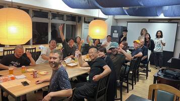 A group of people in a room with tables, chairs, and a projector screen.